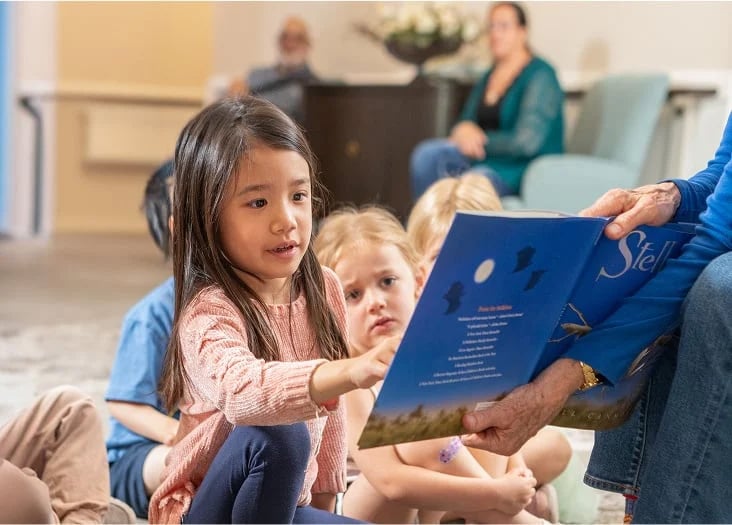 older woman holding a book for a young girl who is reading the book
