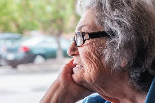 image of senior woman staring out of a window wistfully